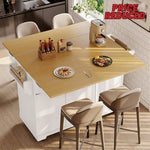 A light wood extendable kitchen island table with white base cabinets, shown in a bright kitchen setting with four beige bar stools. The table is styled with plates of food, a bottle holder, and a coffee maker.
